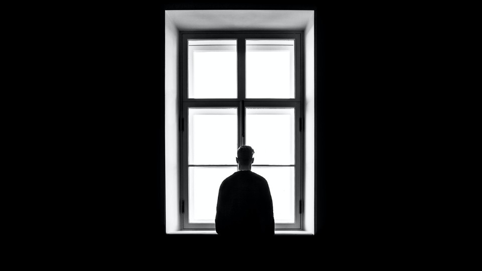 Mann steht alleine vor Fenster.